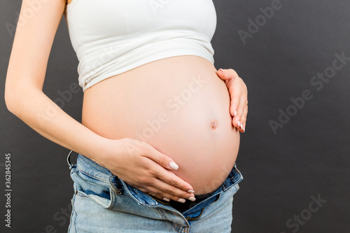 Cropped image of pregnant woman in unzipped jeans showing her baby bump at colorful background with copy space. Waiting for a baby concept © sosiukin