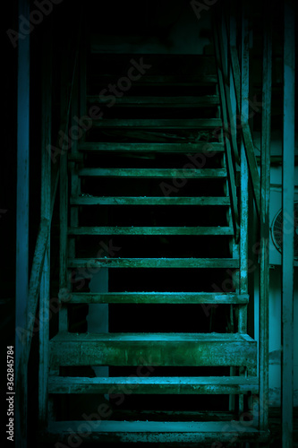 Mystical horror staircase to a dark basement, attic in an old decrepit scary abandoned house with paranormal blue green light and terrible frightening shadows causing fear