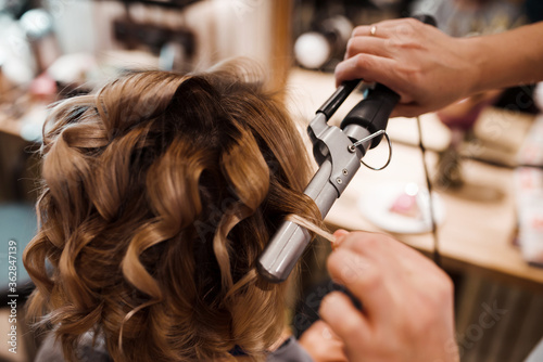 The work of a hairdresser. The master does styling hair and curling with tongs. Close-up of hands and tool