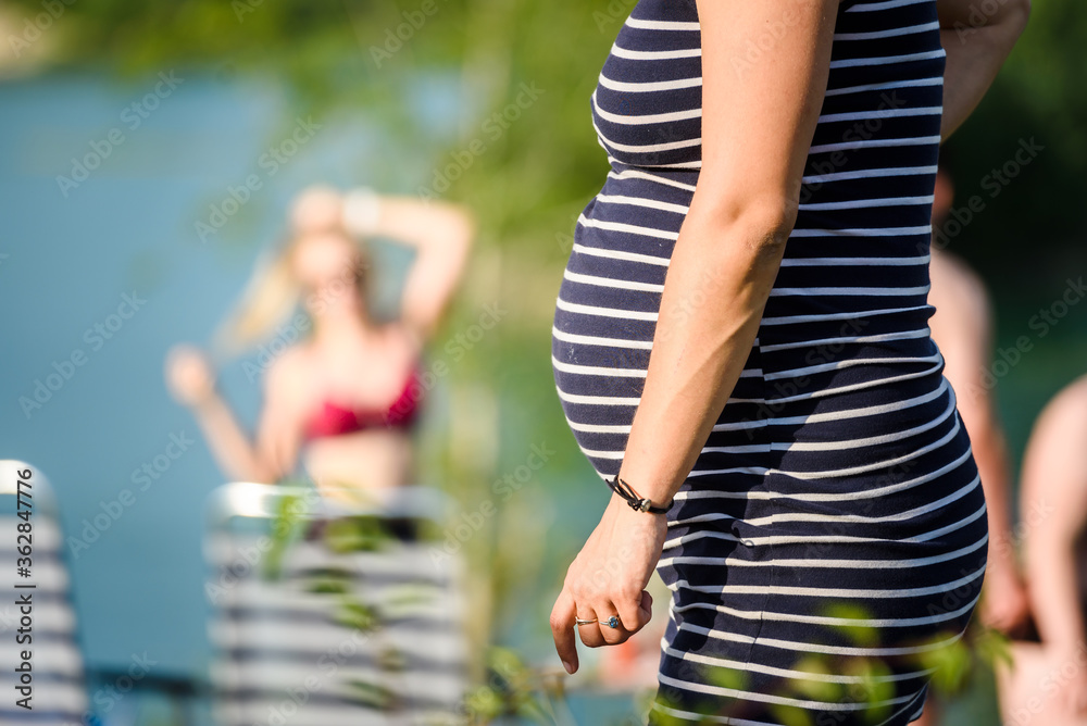 Pregnant woman in a striped dress on the beach. Belly close-up. - obrazy, fototapety, plakaty 