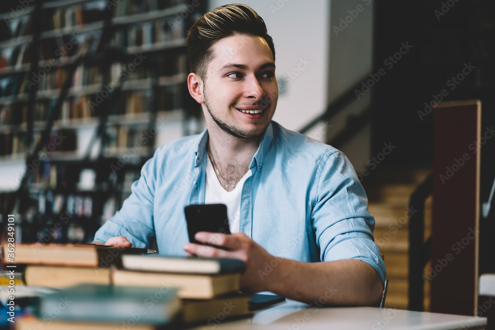 Smiling student browsing smartphone in library Smiling student browsing smartphone in library