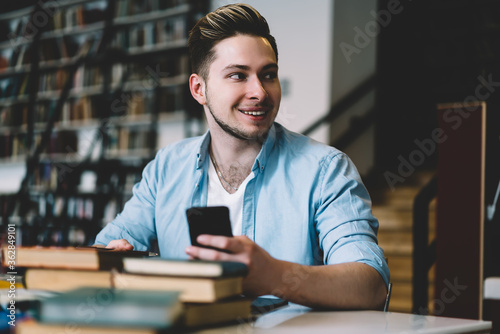 Smiling student browsing smartphone in library