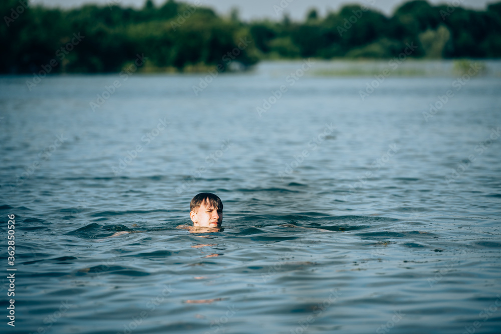 Boy swimming in the lake in summer-view from the back