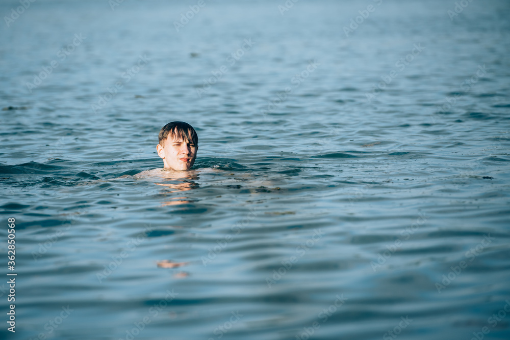 Boy swimming in the lake in summer-view from the back