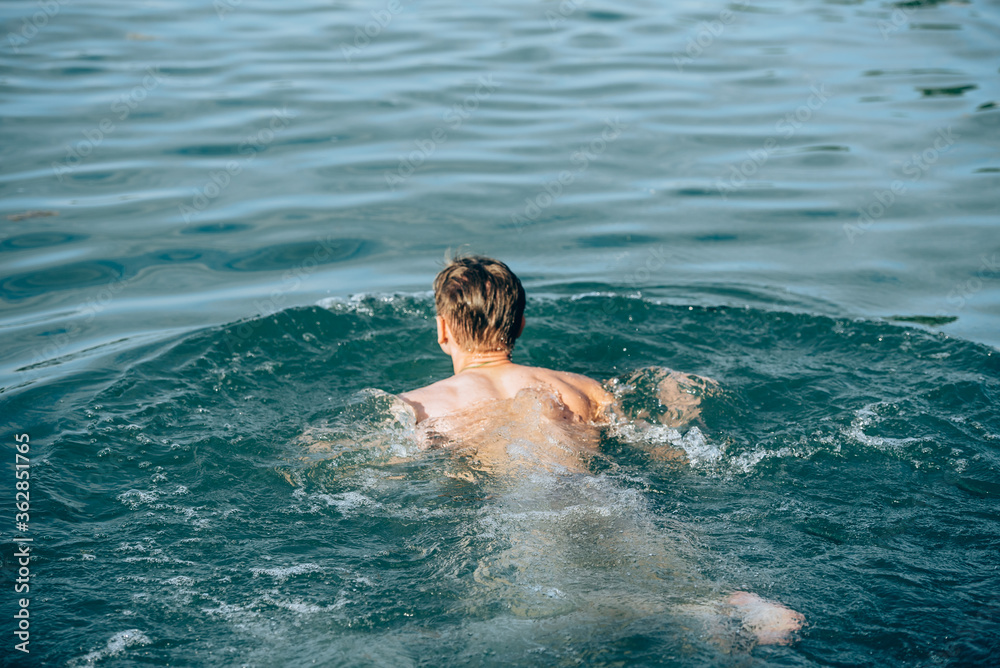 Boy swimming in the lake in summer-view from the back