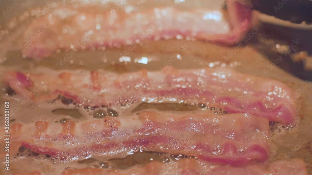 Close up of bacon sizzling as it cooks in a pan in 60 FPS.