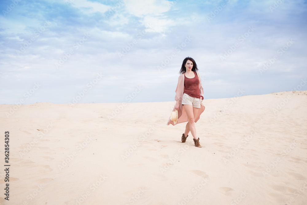 girl in desert walk  with dark hair shorts, sand and blu sky background