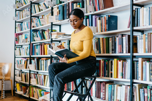 Quadro em tela Concentrated african american young woman in eyeglasses for vision corrective reading literature book preparing for exam