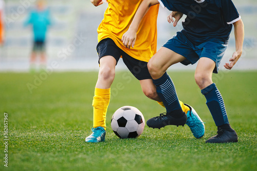 Closeup of soccer players legs in duel. Boys kicking football ball on grass venue. Competition moment between two young soccer football players