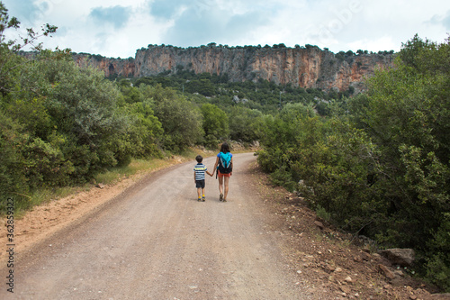 A woman with a backpack leads a child by the hand along a mountain trail.
