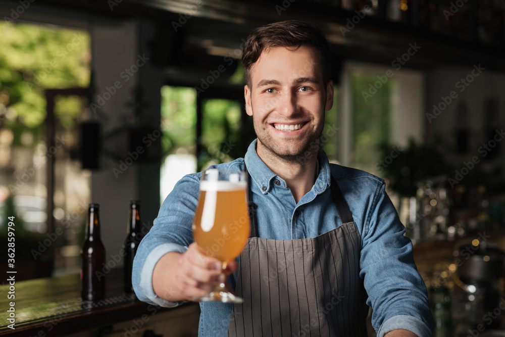 Light lager in glass. Bartender holds out hand with glass of light beer, for client Light lager in glass. Bartender holds out hand with glass of light beer, for client