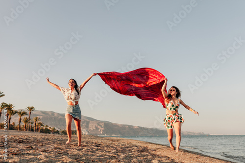 Two women running and holding scarf on wave relax and happy on beach