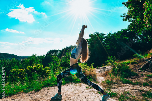 Woman Doing Yoga On Mountain Against Sky and Sun. Hard light. Silhouette of girl doing outdoor sport stretch. photo