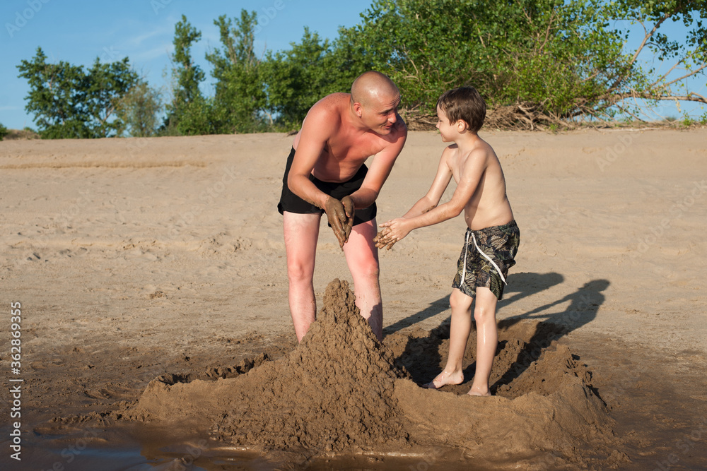 Dad and son build sand castles on the beach and laugh. Photo on the beach on a Sunny day. Family holiday Dad and son build sand castles on the beach and laugh. Photo on the beach on a Sunny day. Family holiday