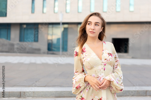 Portrait of a beautiful young girl on a background of a blue business center dressed in a summer beige dress