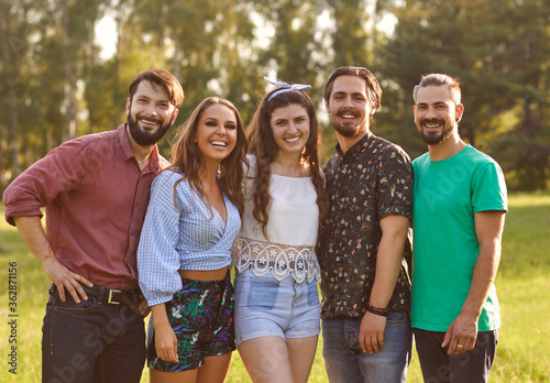 A group of happy friends are looking at the camera while standing in a park on a sunny summer day.