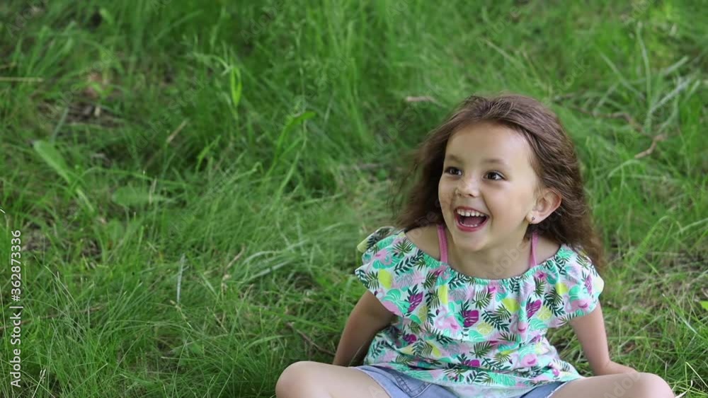 An emotional little girl waves her head and rolls over on her back on a green lawn An emotional little girl waves her head and rolls over on her back on a green lawn