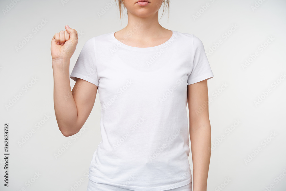 Studio photo of young female with nude manicure clenching fist while showing letter s on sign language, being isolated over white background in white t-shirt Studio photo of young female with nude manicure clenching fist while showing letter s on sign language, being isolated over white background in white t-shirt