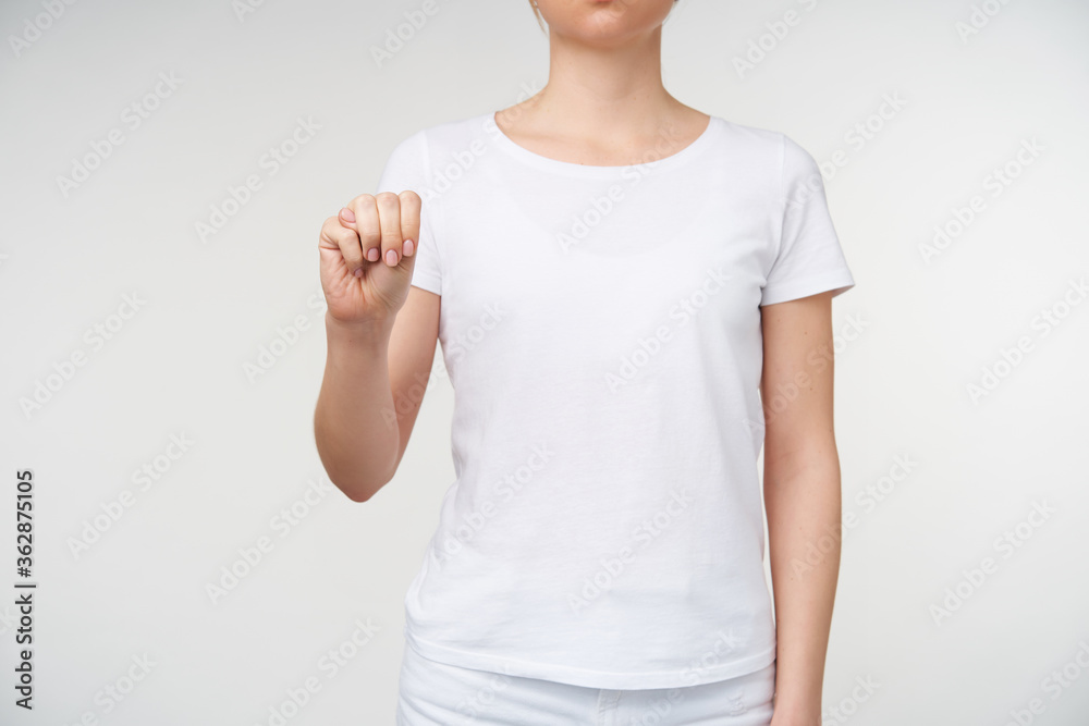Studio photo of young female dressed in white t-shirt clenching her raised hand while forming letter m on sign language, isolated over white background Studio photo of young female dressed in white t-shirt clenching her raised hand while forming letter m on sign language, isolated over white background