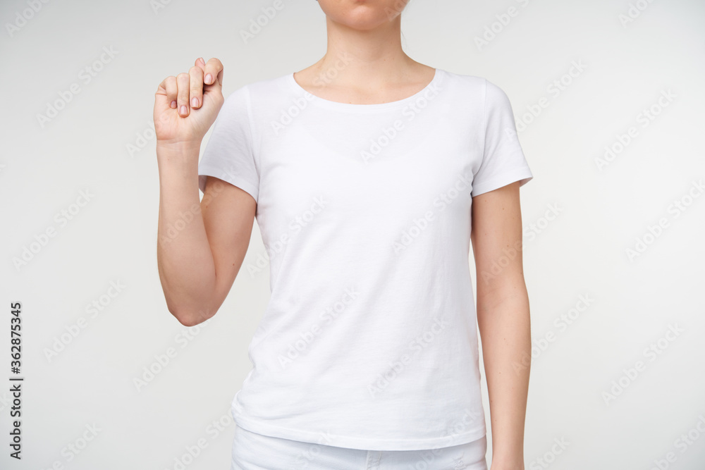 Indoor shot of young woman keeping hand raised and clenching it while showing letter t from death alphabet, standing against white background Indoor shot of young woman keeping hand raised and clenching it while showing letter t from death alphabet, standing against white background