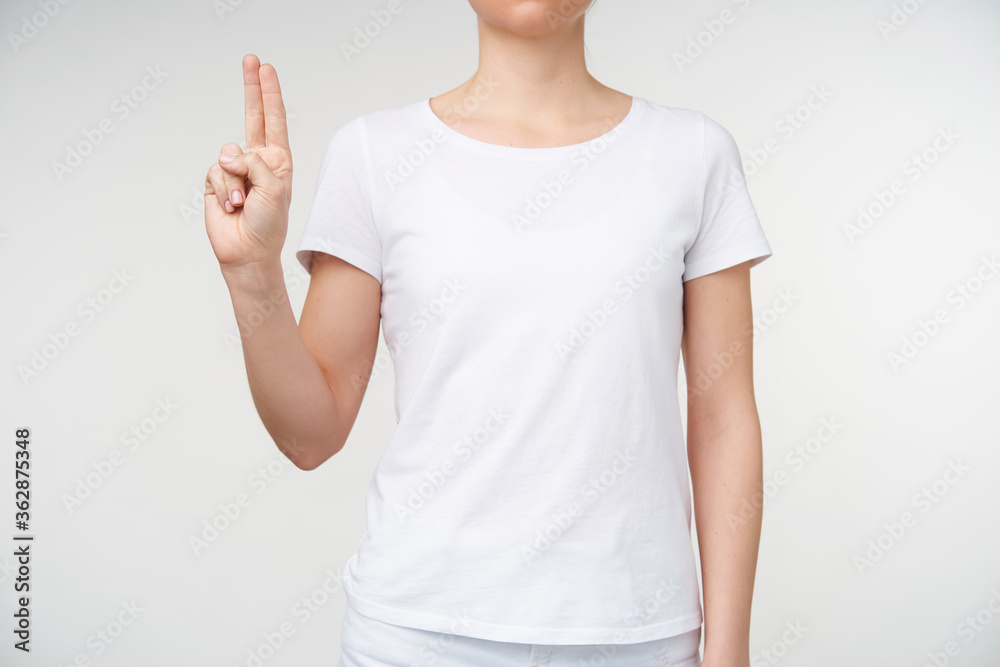 Horizontal photo of young female keeping two fingers together while showing letter u using death alphabet, isolated over white background in casual wear Horizontal photo of young female keeping two fingers together while showing letter u using death alphabet, isolated over white background in casual wear