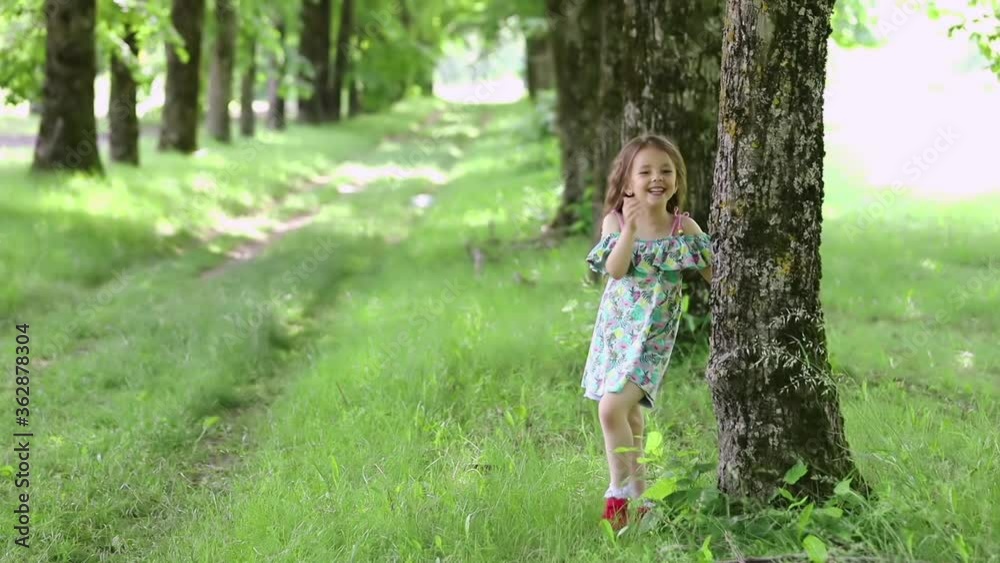 Little emotional girl looks out from behind a tree, laughing and gesturing with her hands Little emotional girl looks out from behind a tree, laughing and gesturing with her hands