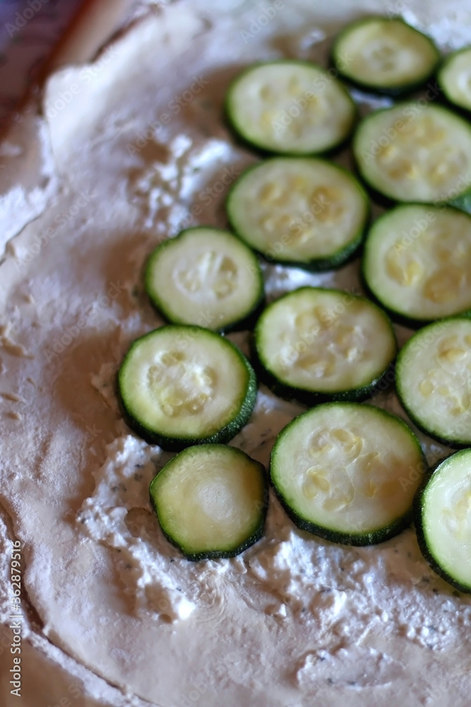 Putting cheese and zucchini slices on a dough while preparing galette. Selective focus.