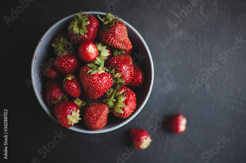 Fresh ripe tasty strawberries in a black plate on a gray wooden background. Two bast bins lie side by side. 