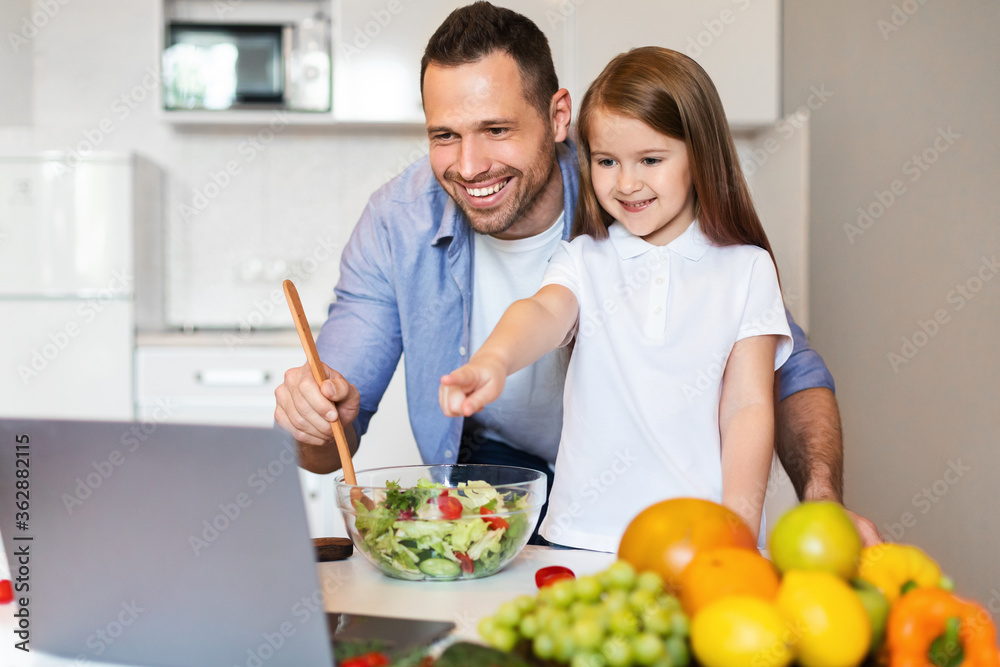 Cute Father And Daughter Cooking Using Laptop Together In Kitchen Cute Father And Daughter Cooking Using Laptop Together In Kitchen