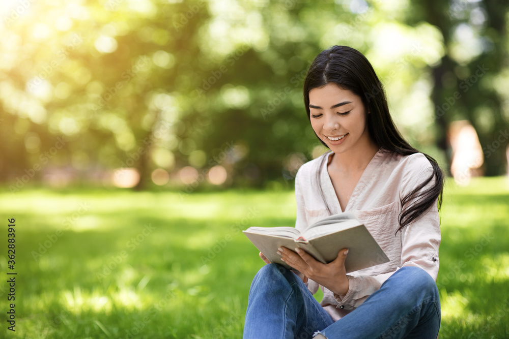 Smiling young asian girl reading book outdoor, relaxing on lawn in park Smiling young asian girl reading book outdoor, relaxing on lawn in park