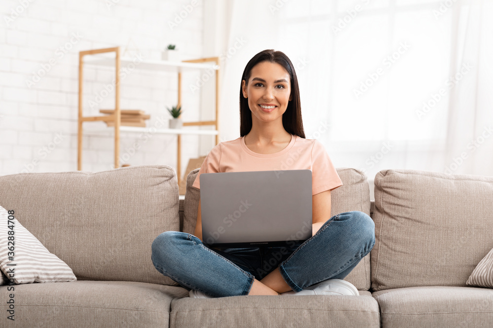 Woman using laptop phone sitting on sofa, looking at camera Woman using laptop phone sitting on sofa, looking at camera