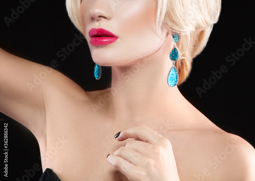 Partial portrait of fashion model woman  red lips  perfect skin  green jewelry earrings. Black background