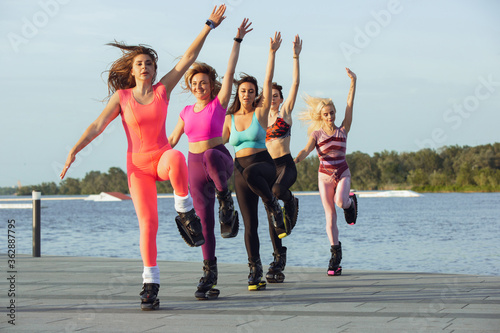 Beautiful women in sportswear jumping in a kangoo jumps shoes at the street on summer's sunny day. Jumping high, active movement, action, fitness and wellness. Fit female models during training. photo