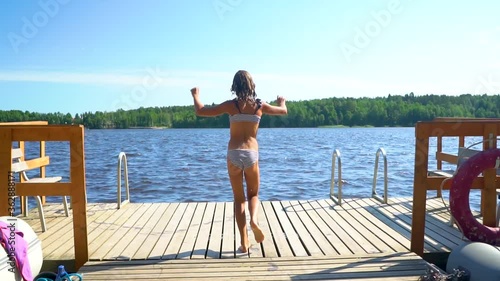 Girl jumping into the lake from wooden pier. Having fun on summer day. Teenager running and diving in to the water.
