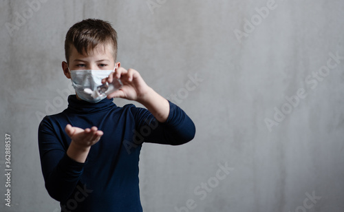 A boy in a medical mask shows how to properly handle his hands with a sanitizer. Hygiene rules during illness concept. Place for text.
