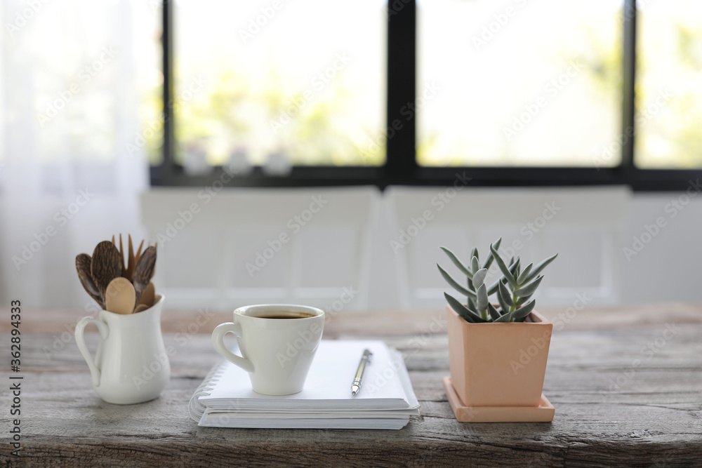 Obraz premium White coffee cup and white notebook and small succulent plant pot with pot of spoons on rustic brown wooden table