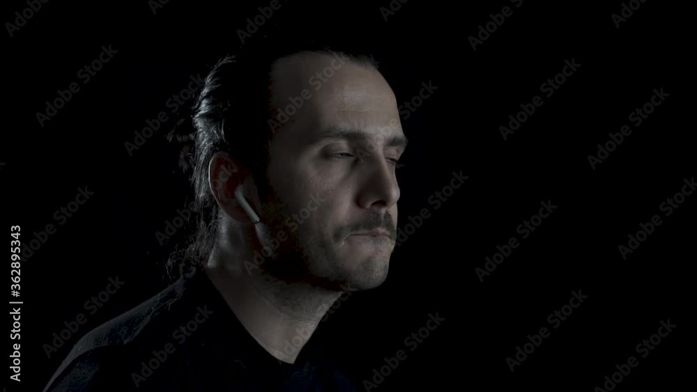 An positive face young man with long haired listening music with Airpods and dancing on black background An positive face young man with long haired listening music with Airpods and dancing on black background