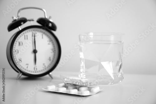 Pills, healthcare and medical concept. An image of a retro clock showing 6:00 am. Water in clear glass, medicine in morning time. Wake up concept, healthy lifestyle.