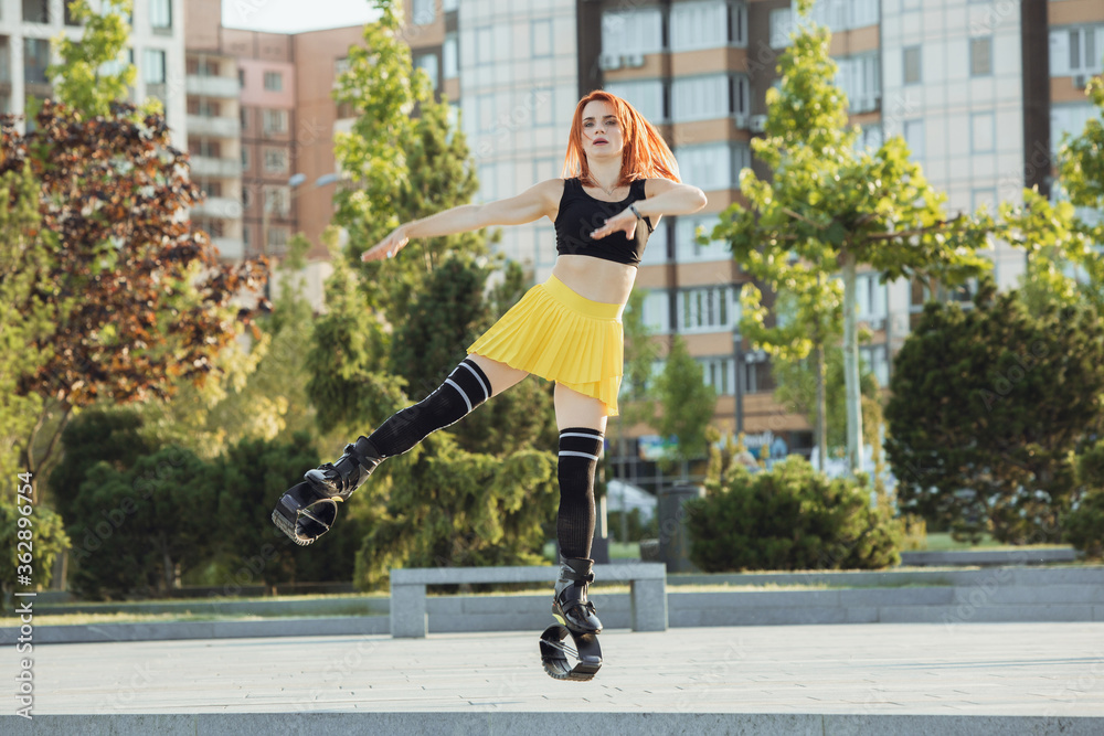 Beautiful woman in sportswear jumping in a kangoo jumps shoes at the street on summer's sunny day. Jumping high, active movement, action, fitness and wellness. Fit female model during training. Beautiful woman in sportswear jumping in a kangoo jumps shoes at the street on summer's sunny day. Jumping high, active movement, action, fitness and wellness. Fit female model during training.