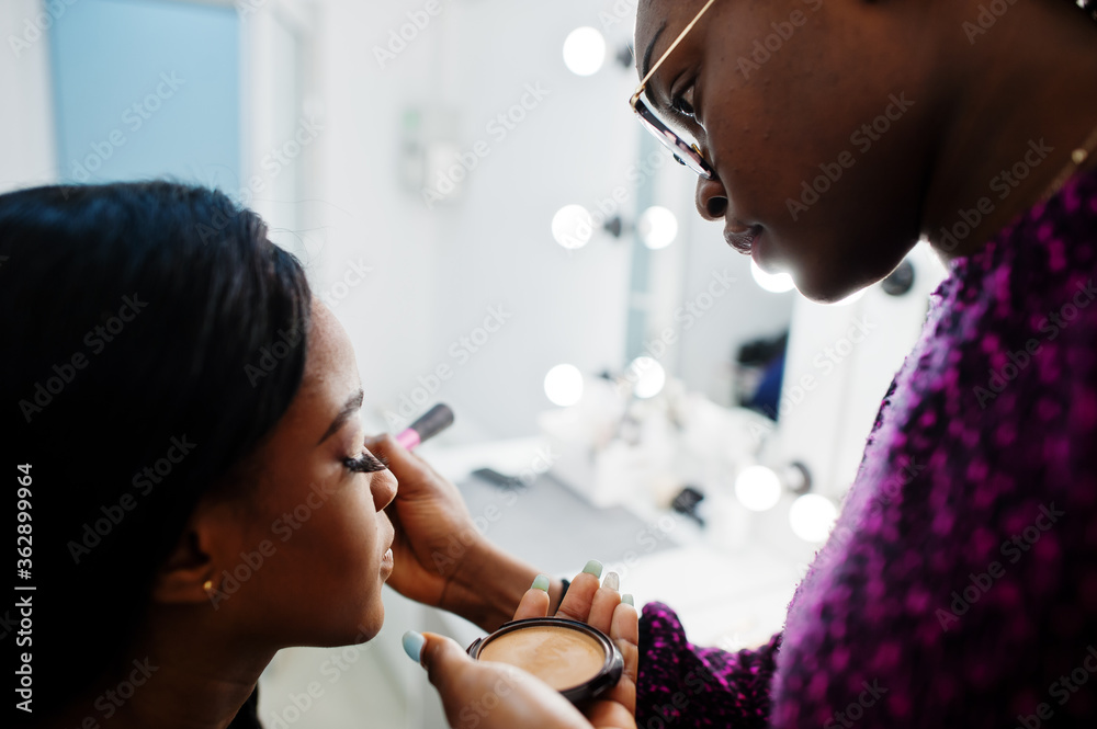 African American woman applying make-up by make-up artist at beauty saloon. African American woman applying make-up by make-up artist at beauty saloon.