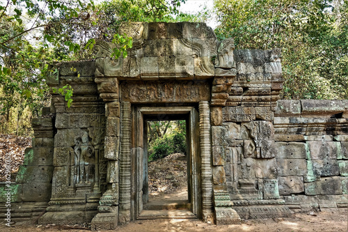Fototapeta Naklejka Na Ścianę i Meble -  The wall of the ancient castle is dilapidated. On the stones are bas-reliefs, carvings, ornaments. The doorway is preserved, this is the passage from the jungle to the jungle. Cambodia, Angkor. UNESCO