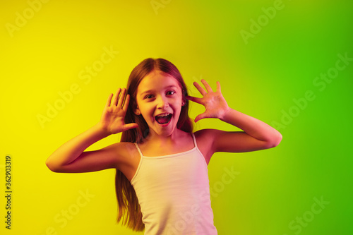 Framing, selfie. Little caucasian girl's portrait isolated on gradient studio background in neon light. Concept of human emotions, facial expression, modern gadgets and technologies, sales, ad