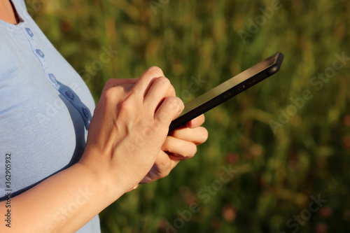 Woman using smartphone on a summer meadow. Close up of female hands with mobile phone on green nature background  concept of sms  online addiction  social media
