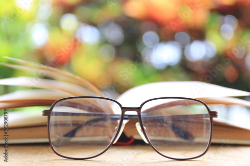 A close up view of old, dusty glasses on the floor Open book in the background selective focus and shallow depth of field