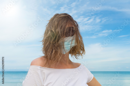 Portret of pretty woman in black sun glasses and medical mask on a face with sea scape background. Safety vacation in summer time. Virus prevention concept. New normal.