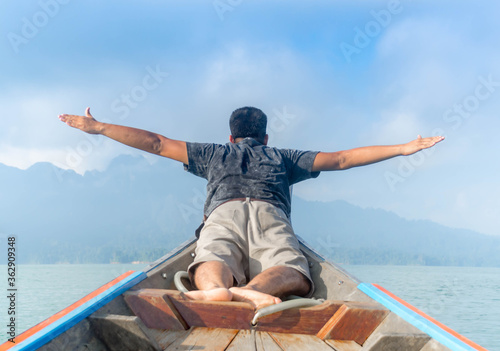 Asian traveler man laying and raising his hands in the air on boat Freedom concept.
