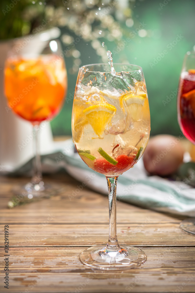 Fresh lemonade cocktail with orange, cherry and ice in wine glass splash on wooden table