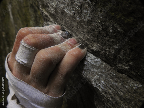 Rock climbers fingers holding on to a crimp on rock, while bouldering, with chalk and tape on hand. Hanging on to the edge of a rock, close-up.