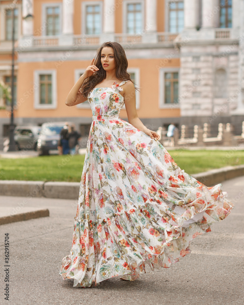 Outdoor fashion female portrait. Elegant woman in long ball gown dress. Caucaisan brunette woman with wavy hair. Girl walking city street Outdoor fashion female portrait. Elegant woman in long ball gown dress. Caucaisan brunette woman with wavy hair. Girl walking city street