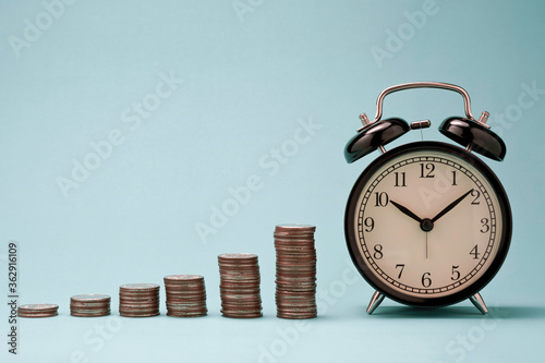 Increase coins stack graph with alarm clock on blue background. Business investment time concept.